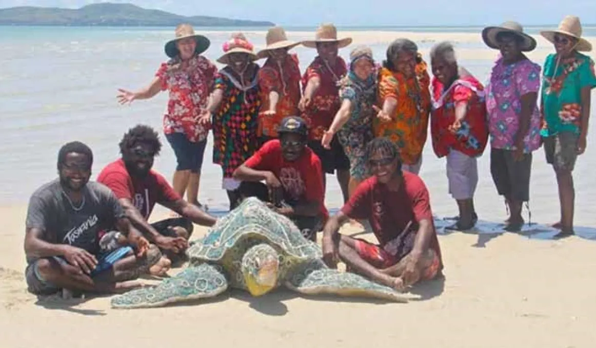 A group of people gather around a large sculpture of a brightly coloured sea turtle.