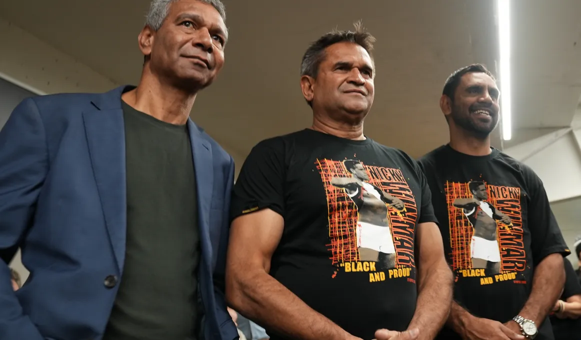 Three Indigenous men stand in a row, smiling.