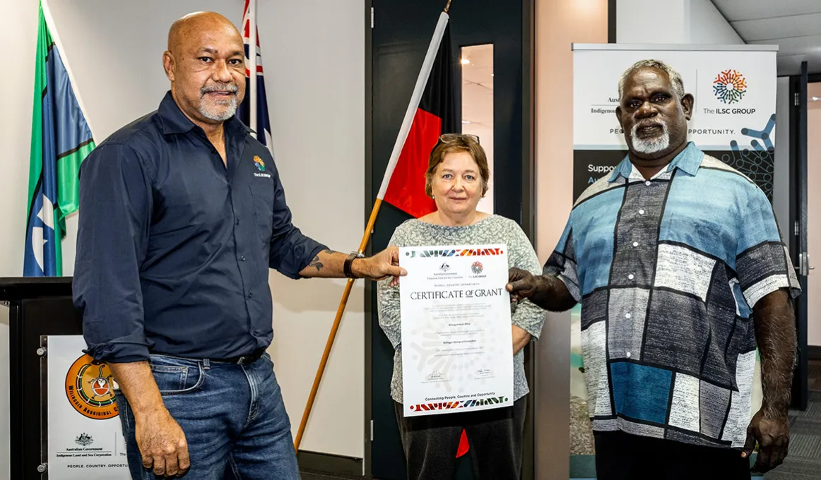 Two men hold a Certificate up in front of a woman in an office