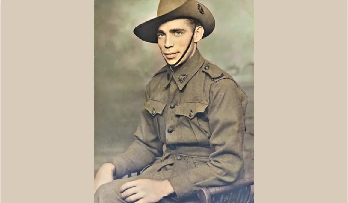 A man in an army uniform sits in a chair. In the background is a painted wall.