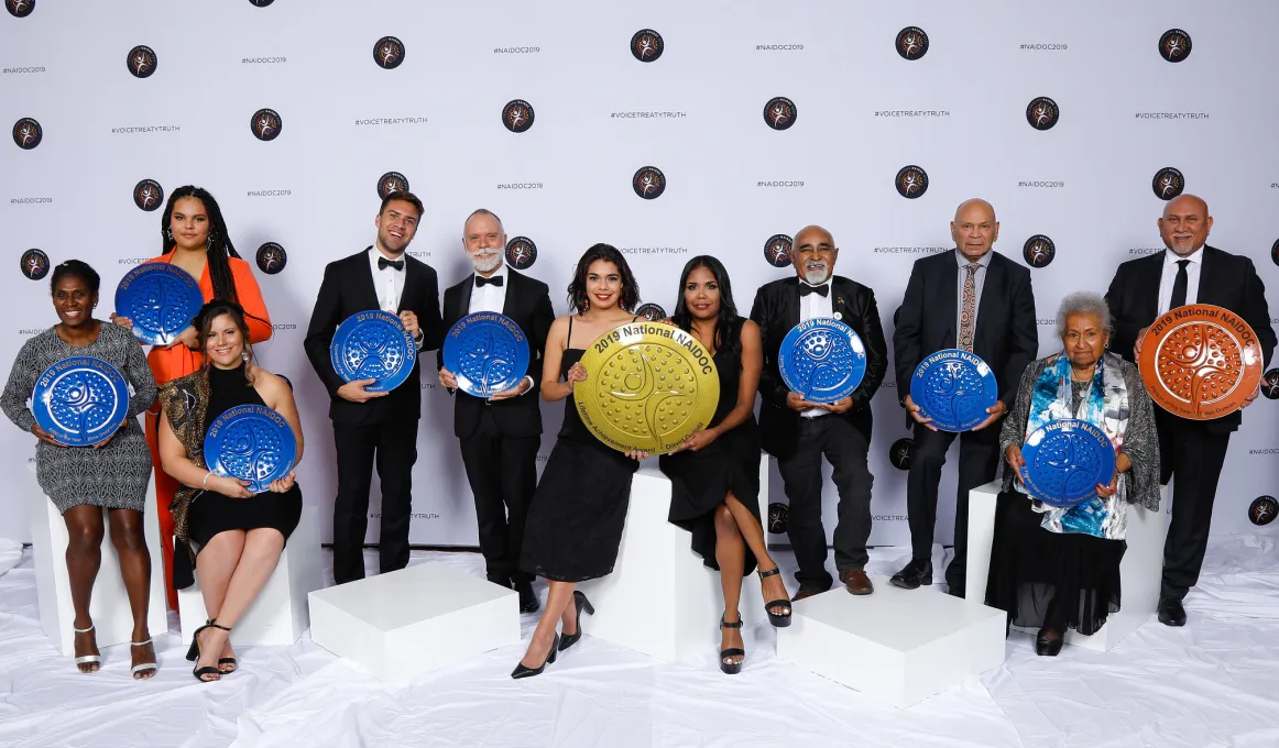 A group of 11 men and women in a row, they each hold an award.