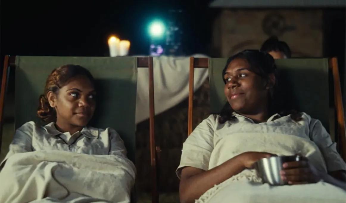 Two Aboriginal woman sitting on decks chairs looking at each other.