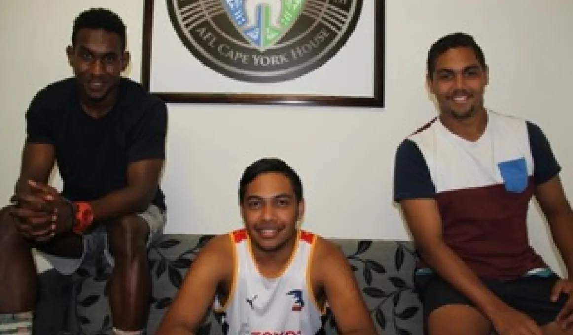 Three young Indigenous men sitting on a couch and smiling.