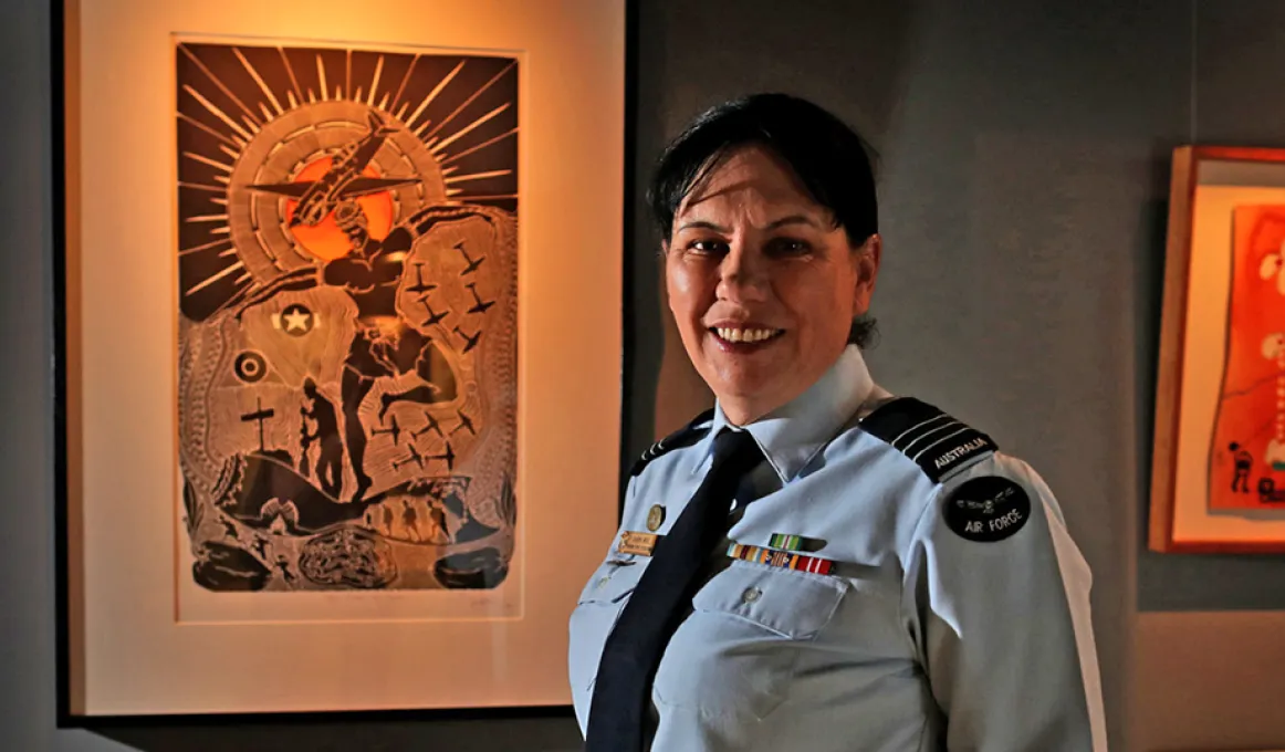 Wing Commander Cheryl Neal dressed in her air force uniform is standing in front of Indigenous artwork.