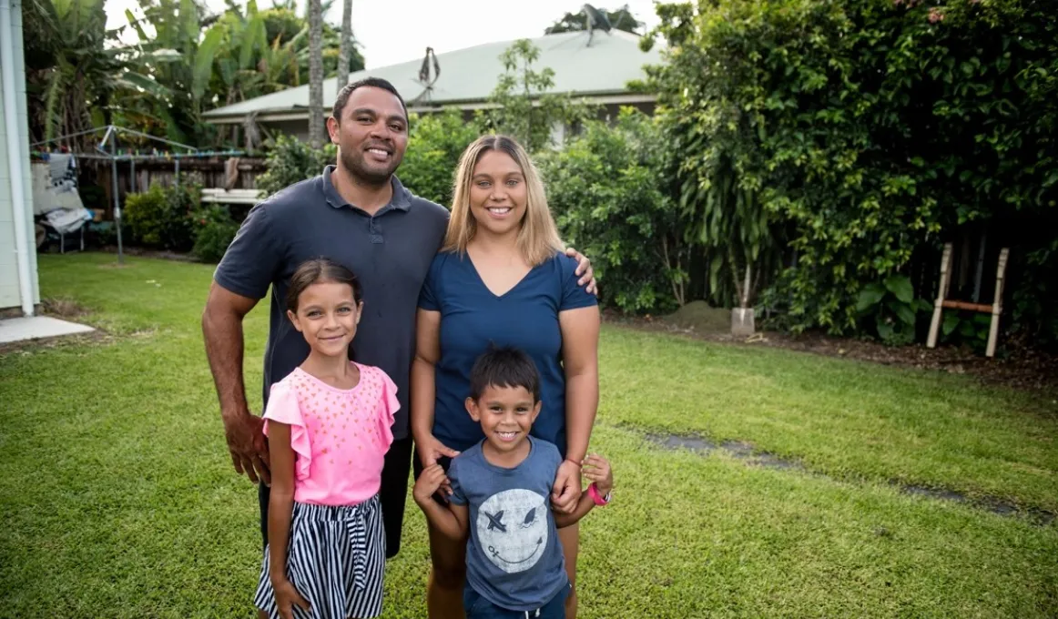 A family photo with a father, mother daughter and son standing in their backyard.