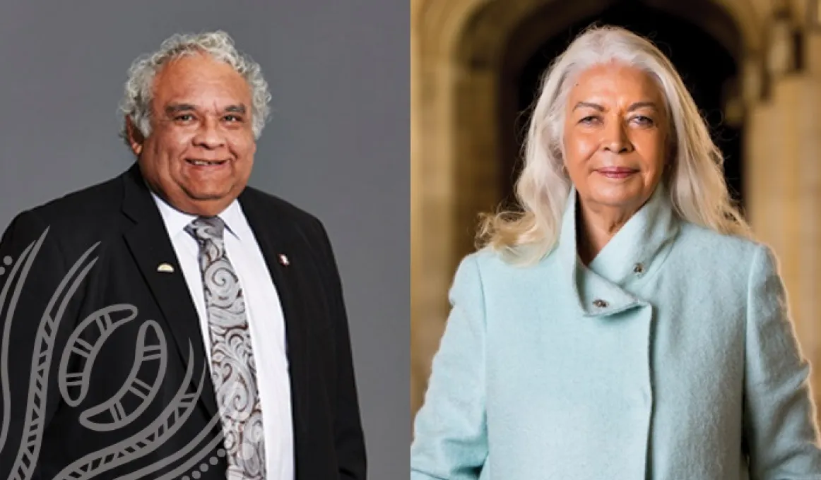 Elderly Indigenous man in suit and tie stands next to elderly Indigenous woman in blue coat.