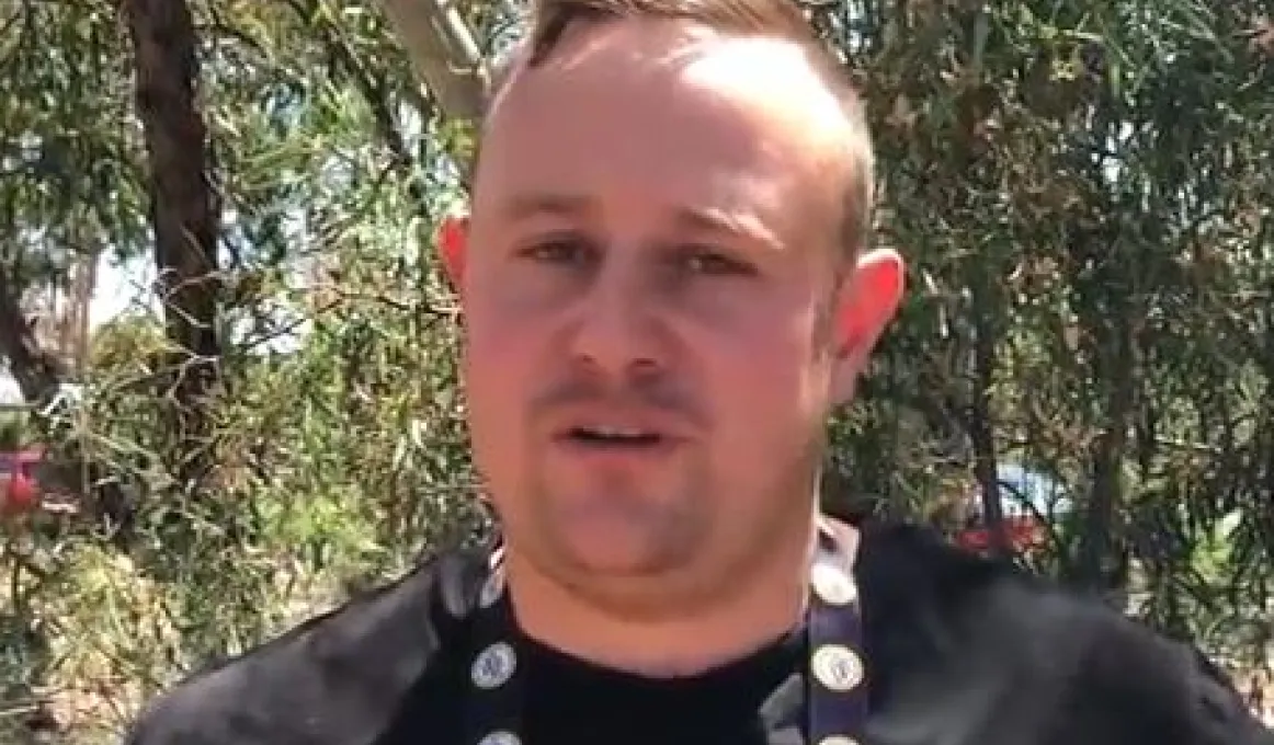 Indigenous man in black shirt stands in front of trees