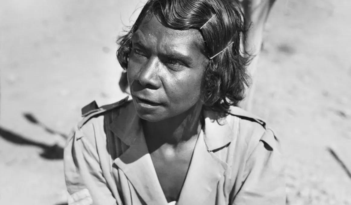 Indigenous woman with hair pinned back wearing army style clothing.