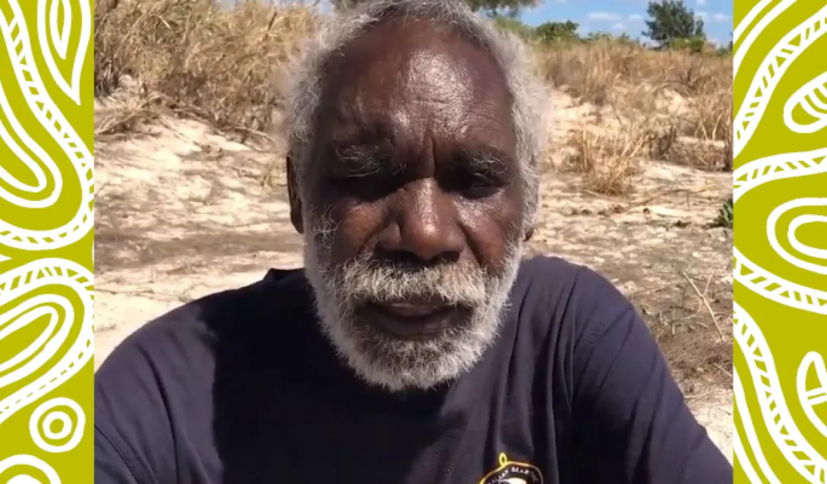 Image of an Aboriginal fisherman sitting on the ground in a dark blue shirt. An orange rectangle with the words “Don Wilton” is in the right hand corner.