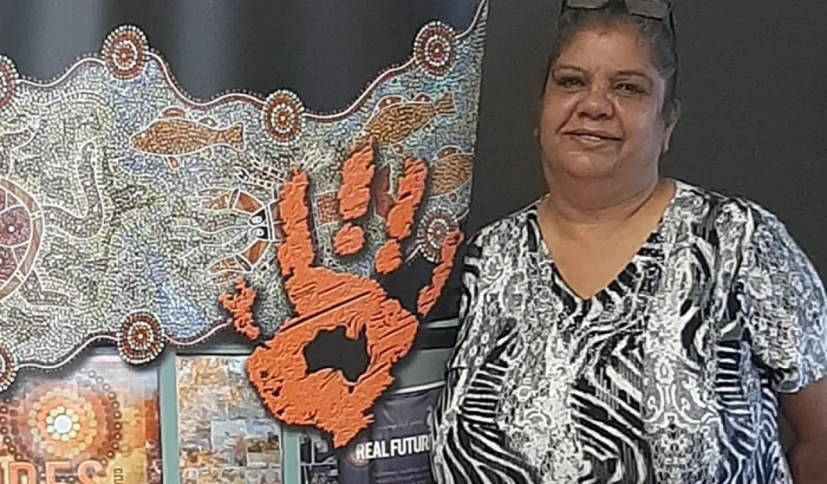 At left is a traditional design featured the imprint of a hand and below are some publications. At right is a woman with glasses on her head and she wears a black and white dress with Aboriginal designs.