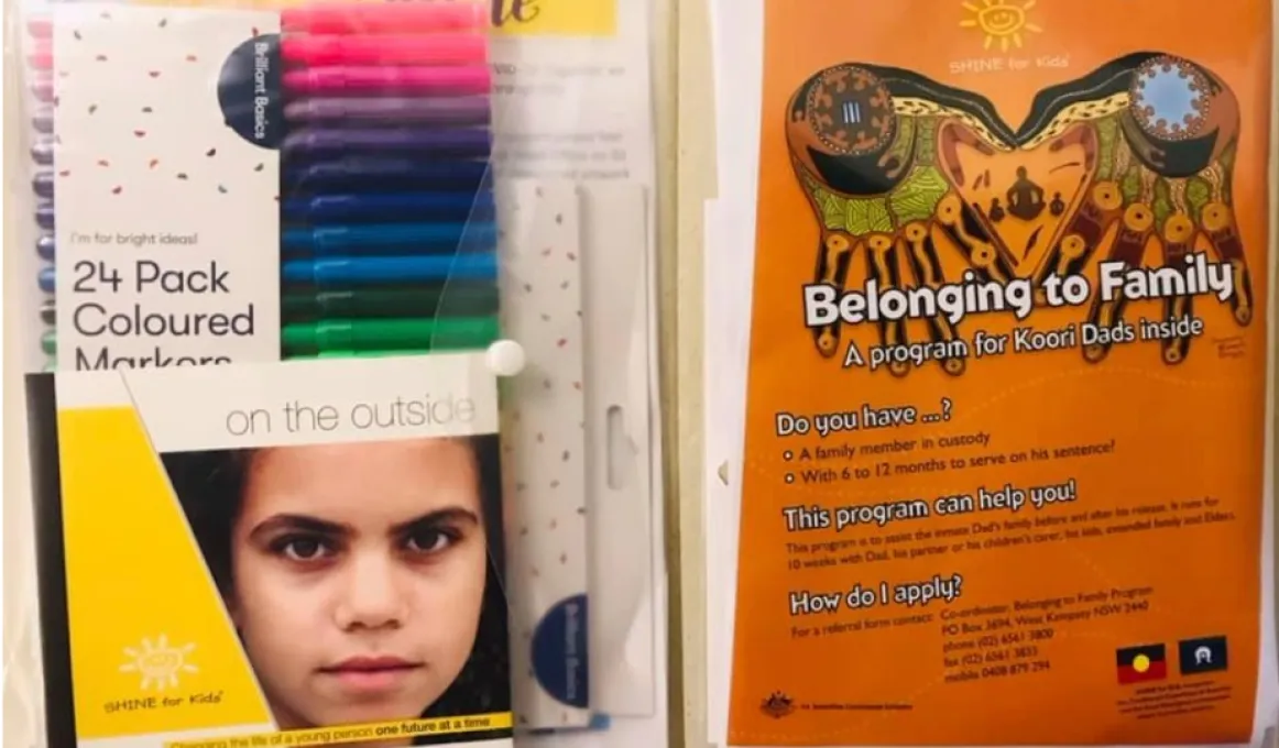 Image of 2 plastic bags filled with paper items. At left, the bag is filled with a pack of pens and a booklet featuring a young girl in the cover. At right, the bag has an orange poster featuring a traditional design and text including Belonging to Family