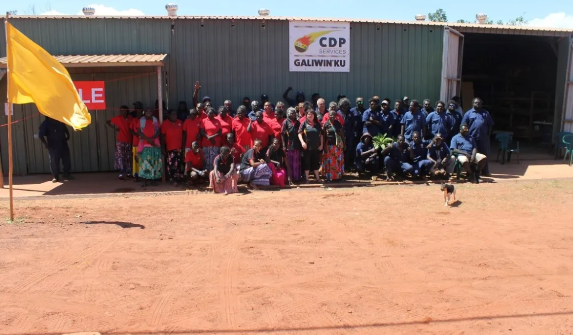 A large group of Aboriginal people standing out the front of a large shed.