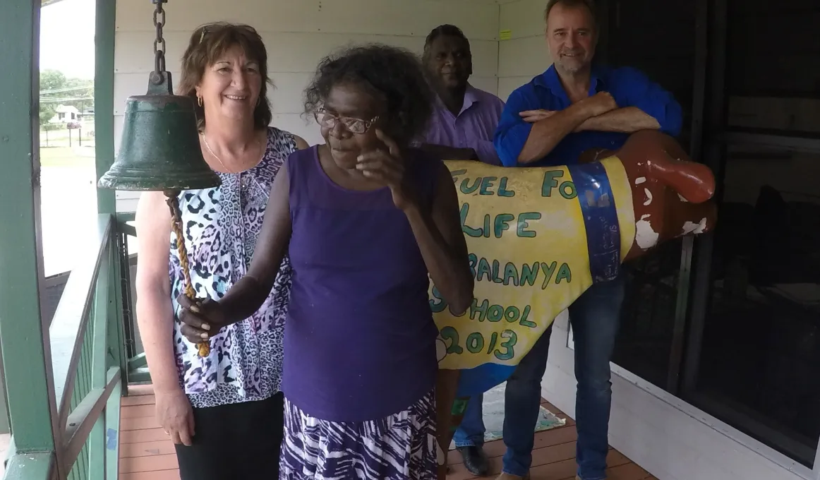 An Indigenous woman ringing a bell in foreground with three people behind her.