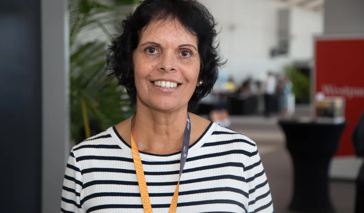 Indigenous woman with dark hair and white shirt with thin navy stripes smiling at Darwin Indigenous Trade Fair.