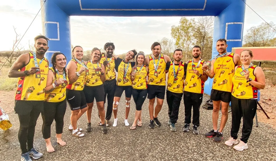 Group of people stand in a semi circle. They are dressed in running clothing and wear a yellow singlet with a medal around their necks.