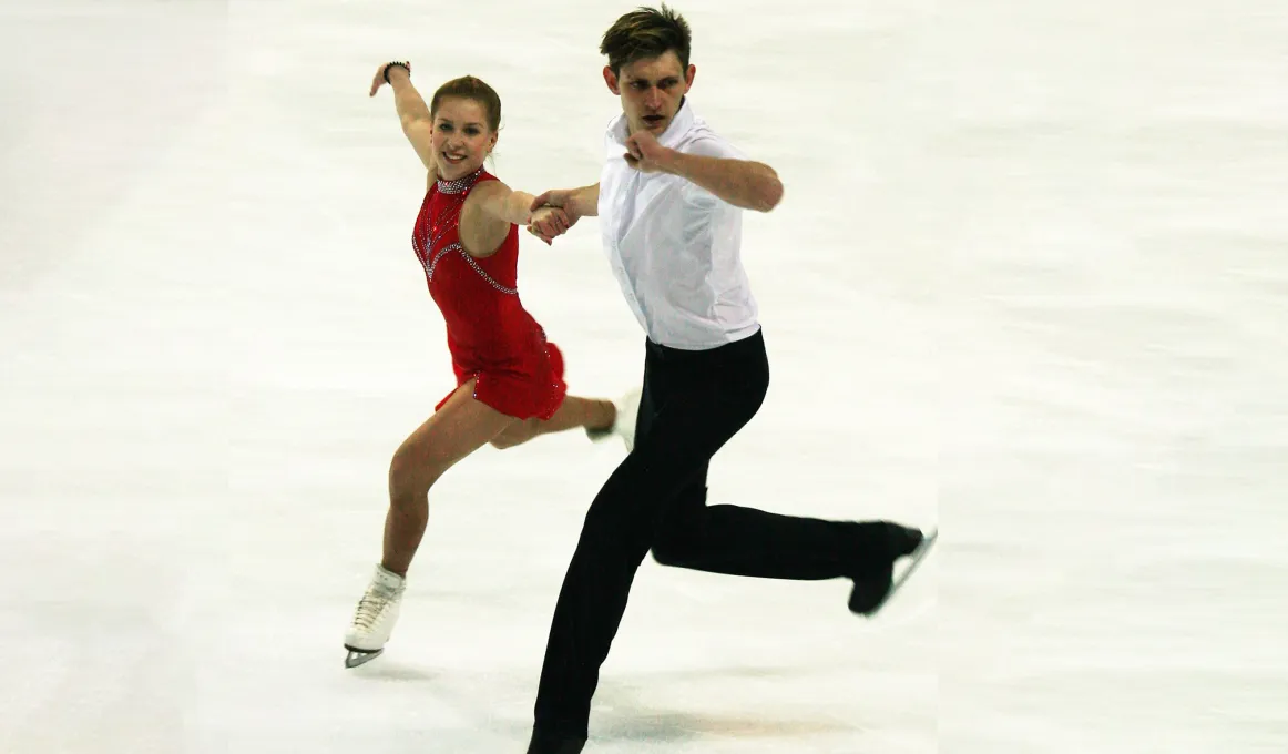 Young woman in red dress holds hands and skates with Indigenous young man in white shirt and black pants.