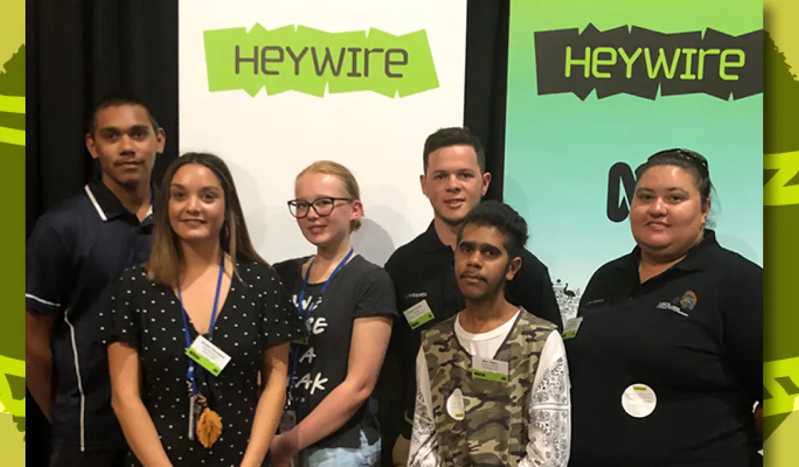 Six young people stand in front of two pull-up banners.The banners both have the word ‘Heywire’ written on them.