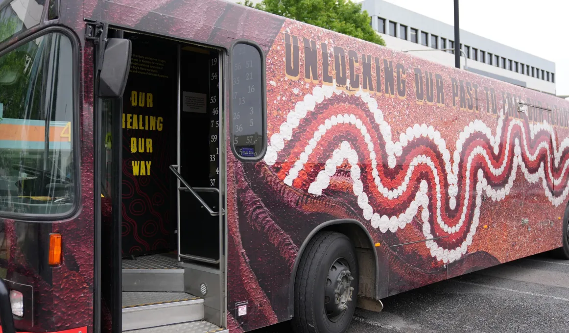 Image of a bus parked outside an office. It is painted with an Indigenous style design.