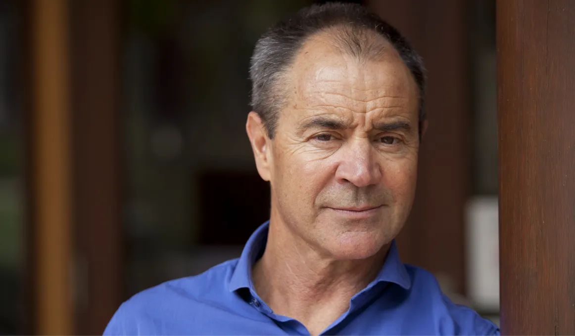 A man in a blue business shirt leans against a vertical timber support beam. He is smiling.