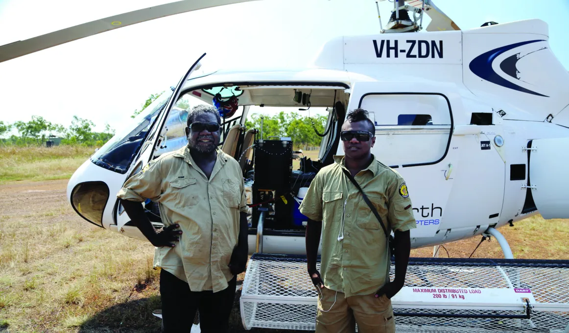 Two indigenous men standing in front of a helicopter