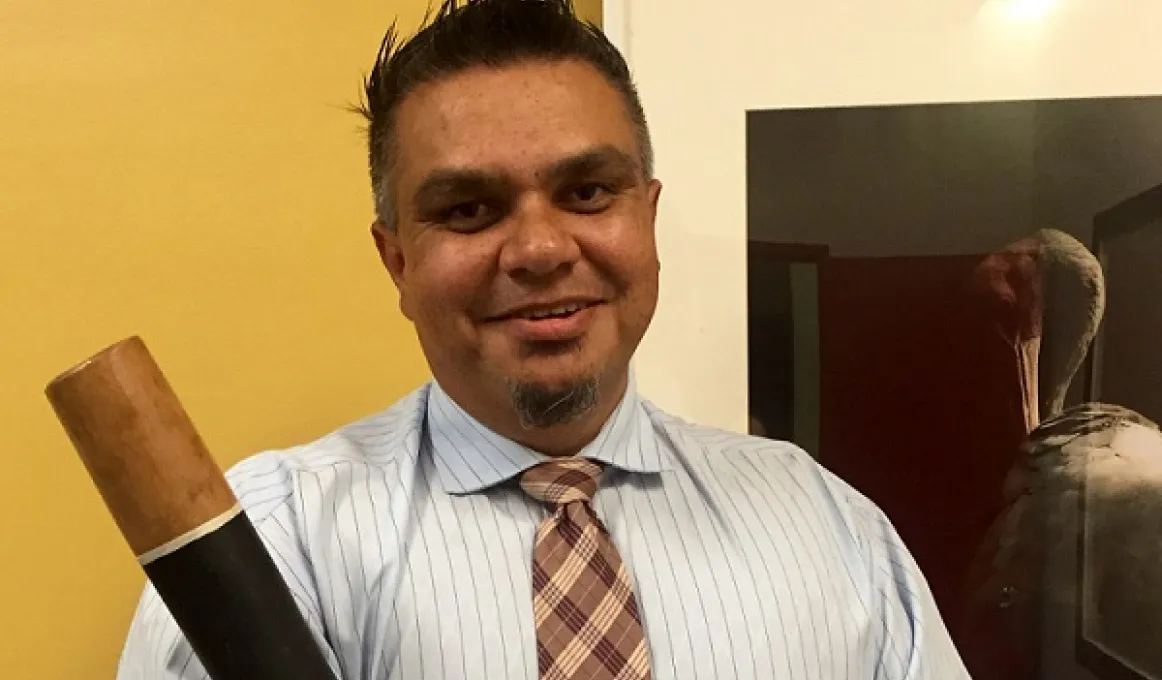 Aboriginal man dressed in shirt and tie and holding a didgeridoo.