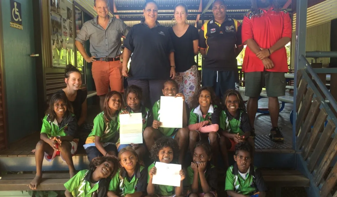 A group of Aboriginal school students sit on steps, holding a letter from the Prime Minister the Hon. Malcolm Turnbull, MP. Behind them stand five adults.