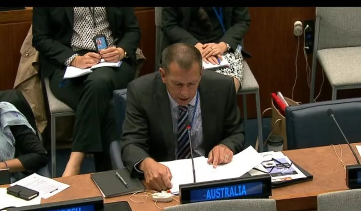 Mike Fordham reading from a text while seated at a bench in the United Nations general assembly room