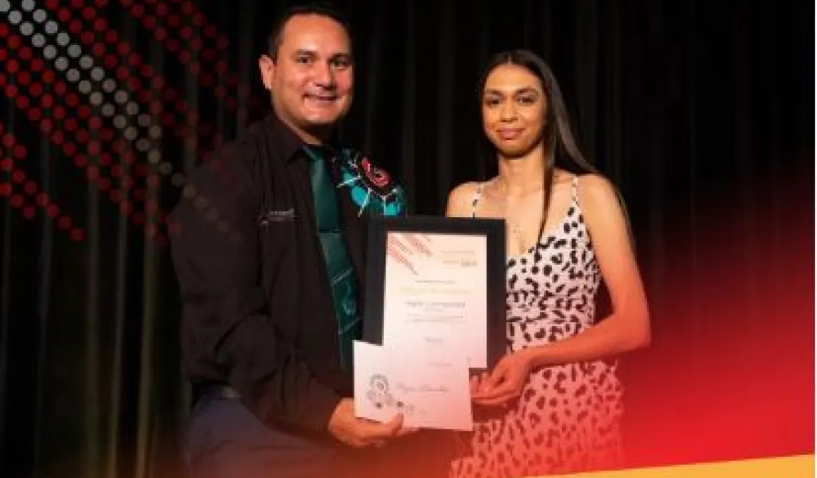 A man in dark shirt and green tie at left and a woman in black spotted white dress at right. Both hold and display certificates.