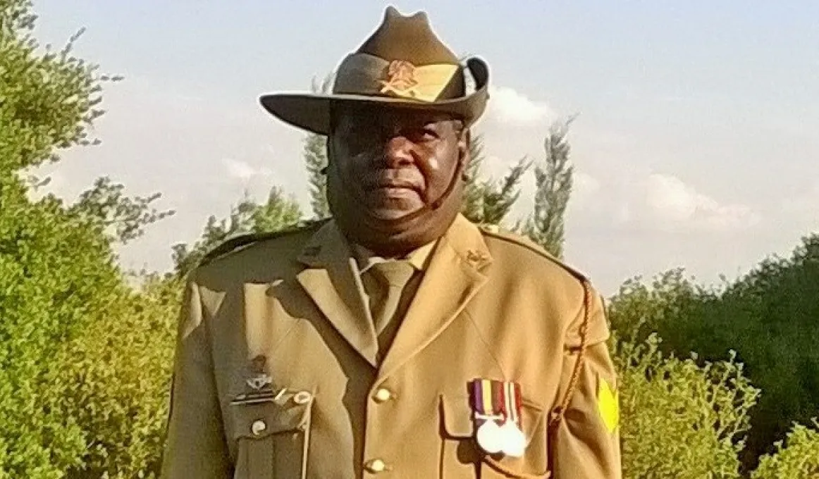 Aboriginal man in full army uniform standing with trees in the background.