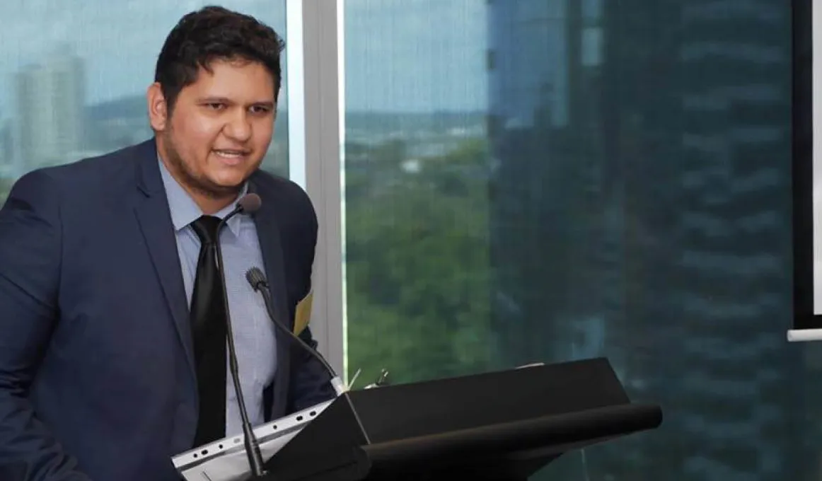 A young Aboriginal man wearing a suit and tie is speaking at a rostrum.