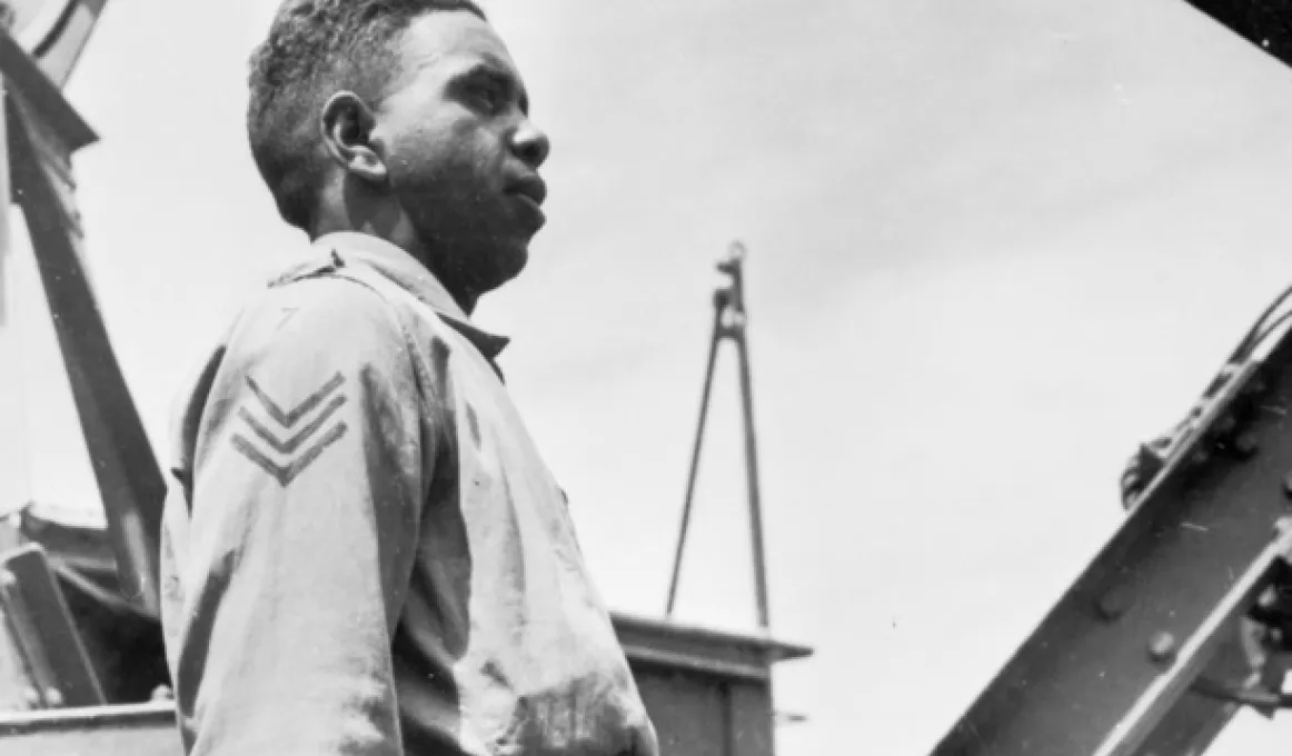 Black and white archive photo of Reg Saunders, an Indigenous man, wearing an Australian Army. He is outside and pictured in profile, facing right.