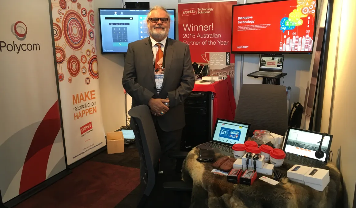 Indigenous man in suit standing amongst display of posters and technical equipment.