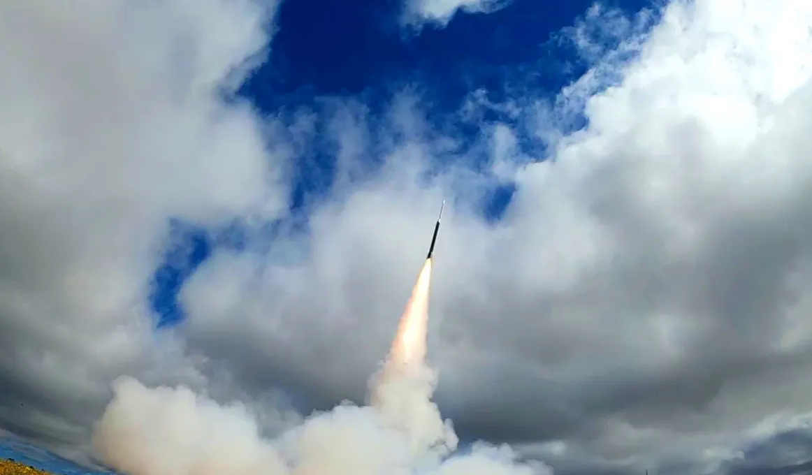 A rocket with a gas trail behind it heads toward a sky with a bit of blue but mainly cloudy.