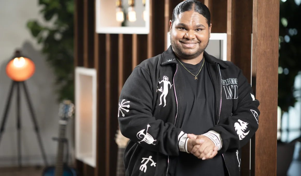 Australian Idol winner Royston Sagigi-Baira, a Torres Strait Islander man, wearing a black t-shirt and black jacket. He is smiling at the camera.