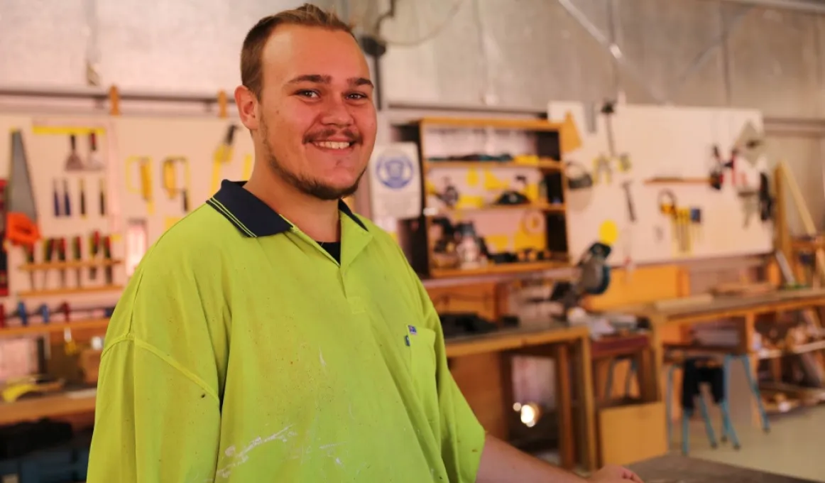 Man in safety vest stands in wood workshop