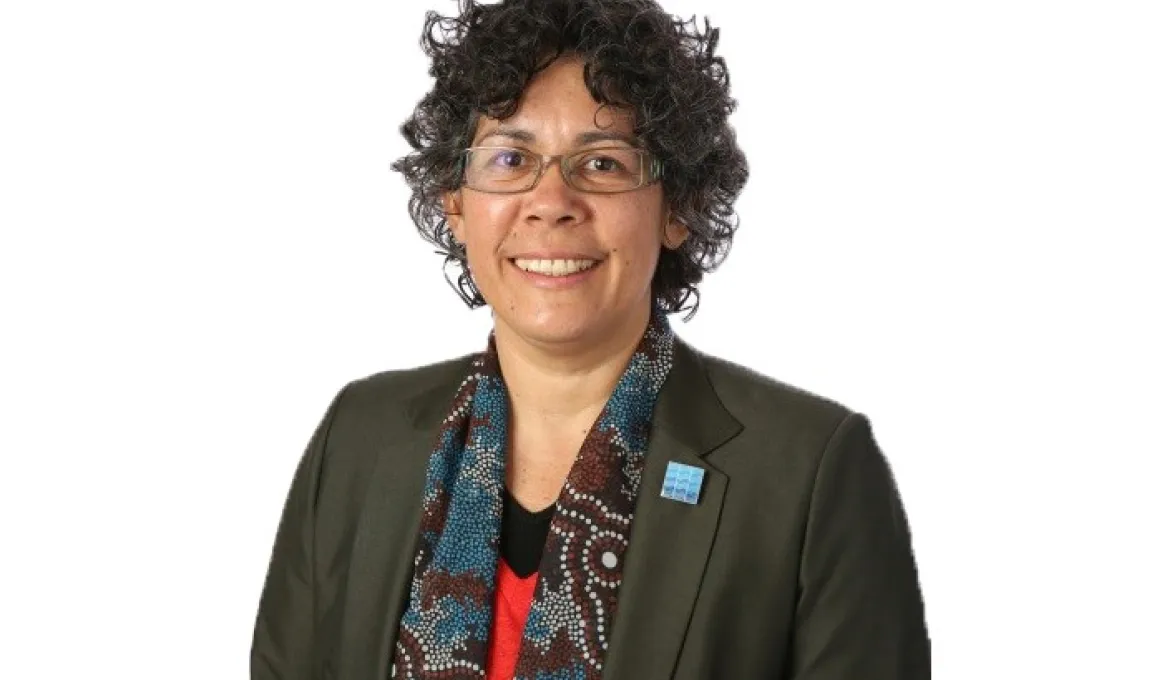 Aboriginal woman wearing glasses, a dark jacket and scarf covered with Indigenous designs.