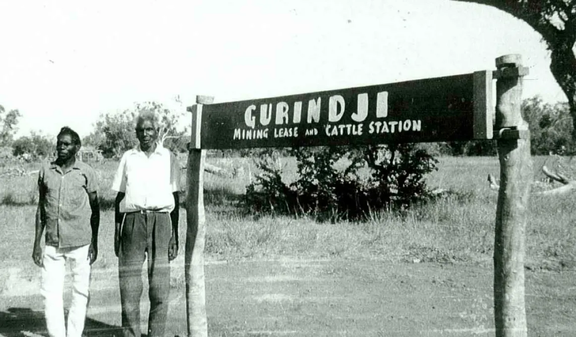 Black and white photo showing strikers Vincent Lingiari and Mick Rangiari in front of a sign that says 'Gurindji Mining Lease and Cattle Station'.