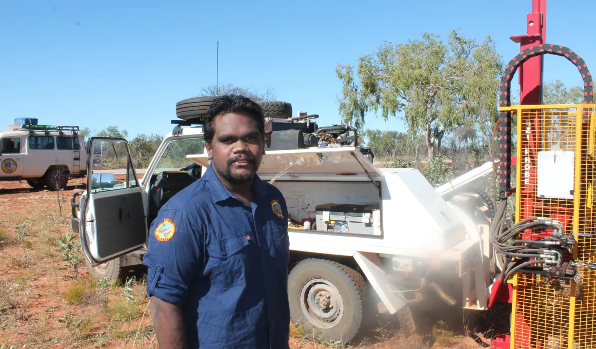 A young Aboriginal man, Wynston Shovellor-Sesar, stands in front of vehicle and other machinery.