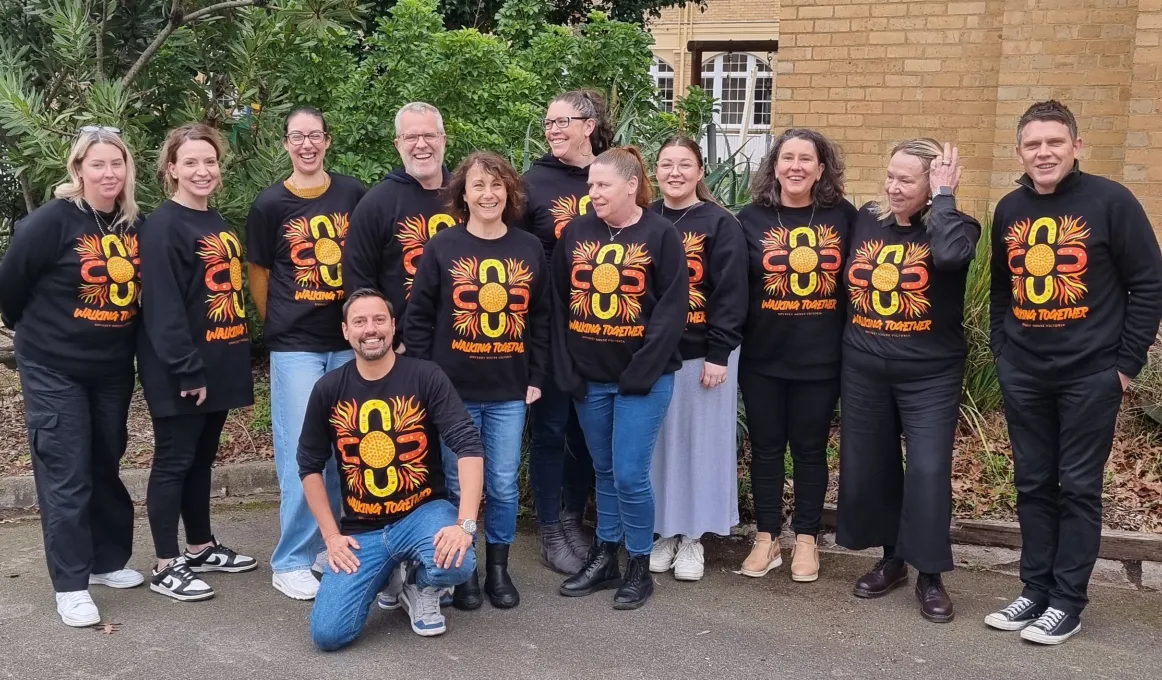 A group of smiling people wearing shirts with a matching brightly coloured design and the text 'Walking Together'