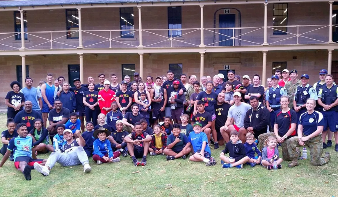 Large group of Indigenous youth and young adults and police officers sit and stand on a lawn in front of a two-storey building.