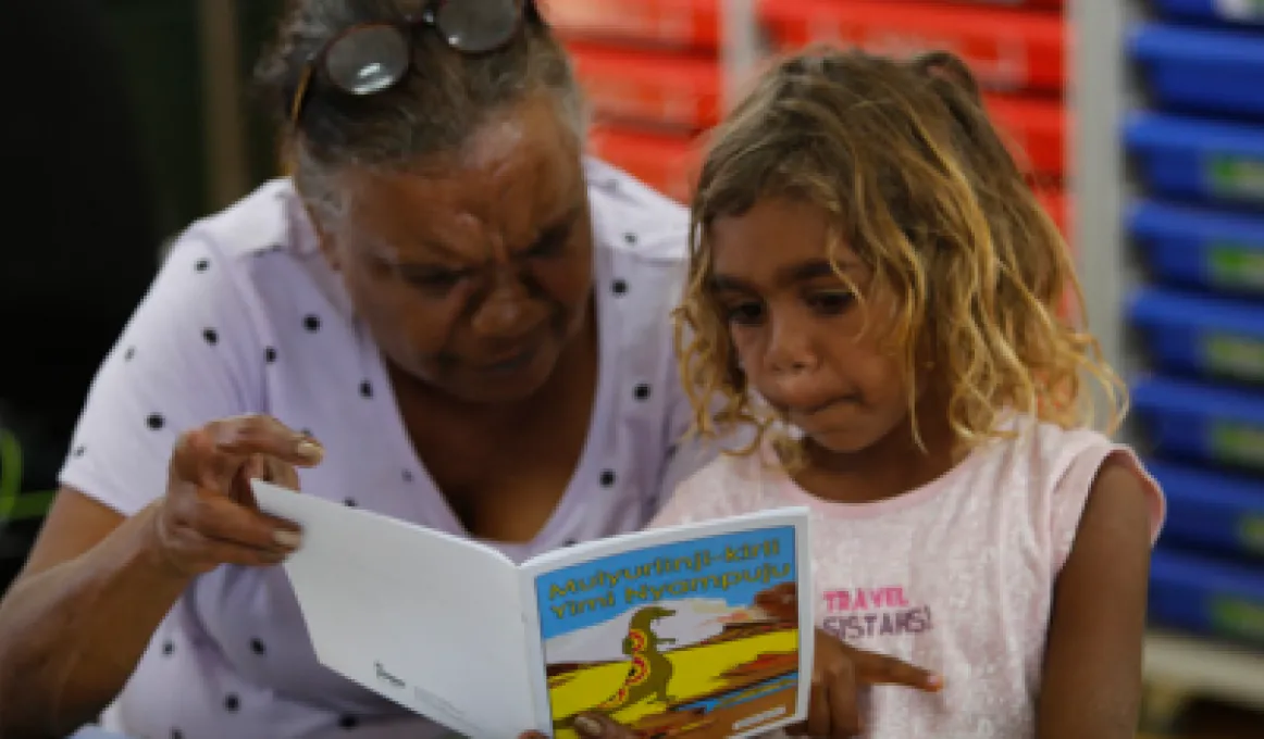 A mature woman and a young girl hold a picture book between them and read.