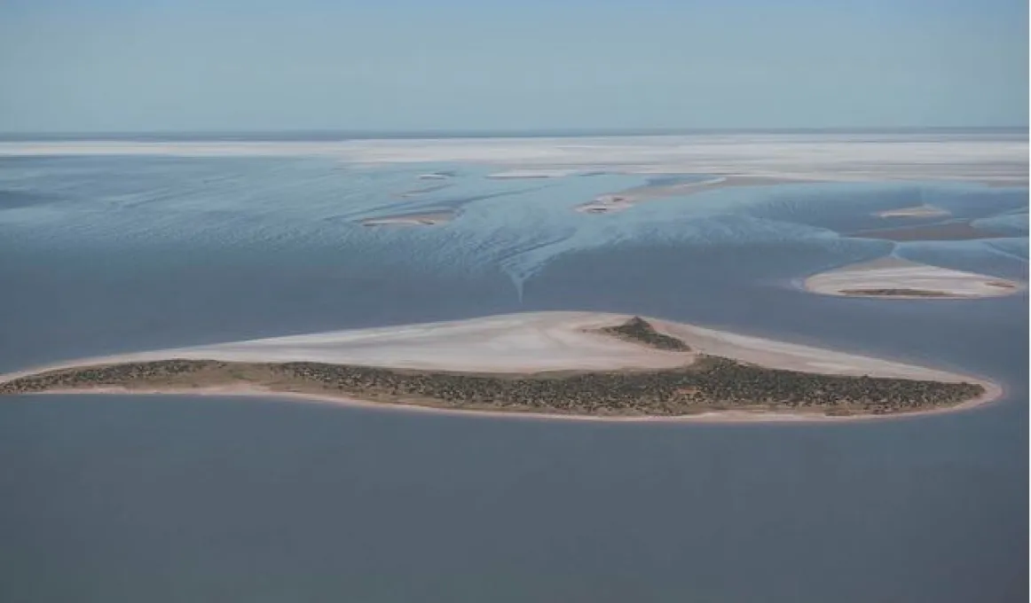 A large expanse of water is populated by low lying sandy islands with the edge of a salt pan in the distance just below the horizon.