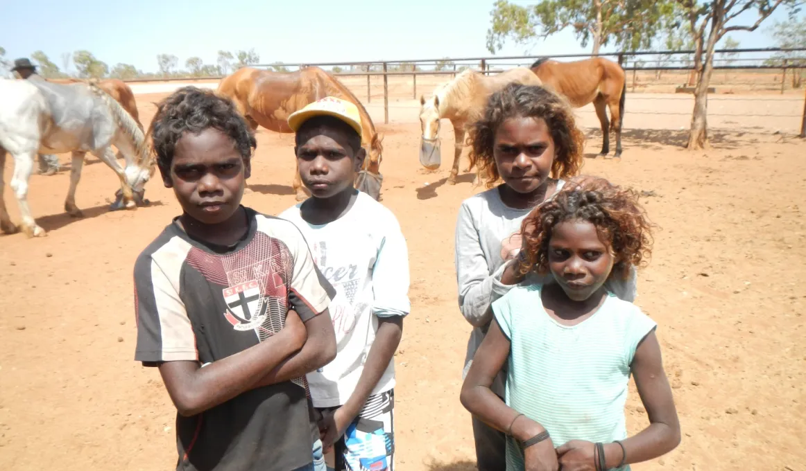 Four children standing in yard with horses behind them