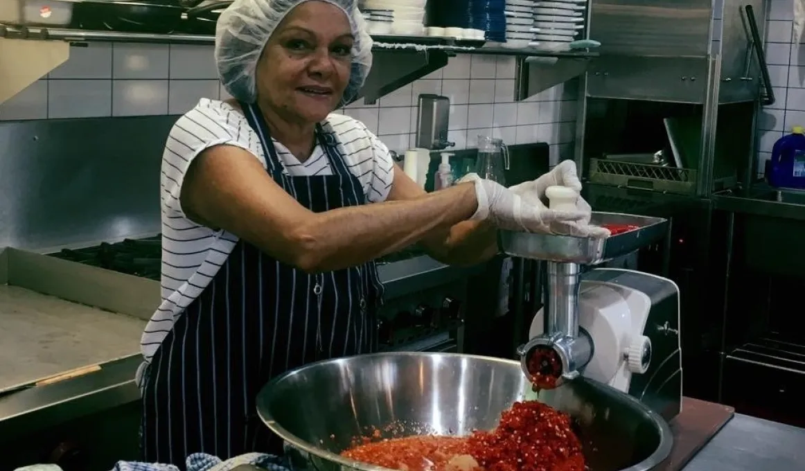 Middle aged Aboriginal woman in an industrial kitchen, making chilli with the help of kitchen appliances.