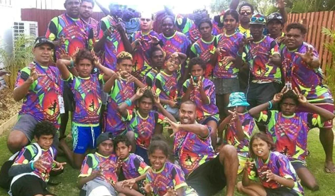 Aboriginal adults and youth in colourful shirts sitting on grass.