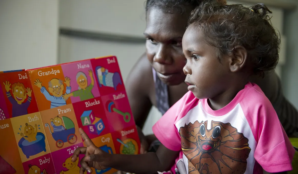 Aboriginal woman and young girl read a colourful child’s picture book together.