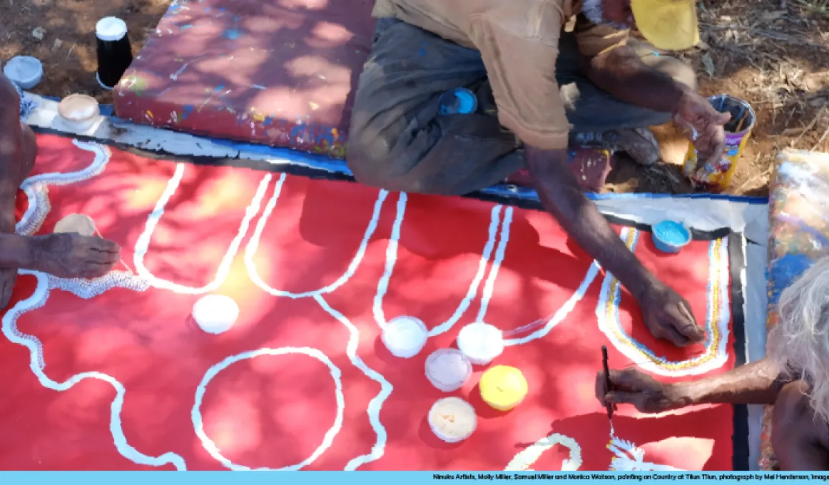 Three Indigneous artists working on a painting.