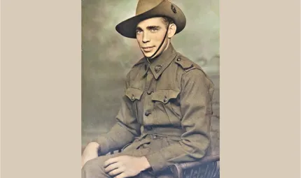 A man in an army uniform sits in a chair. In the background is a painted wall.