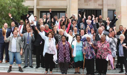 Group photo of people, some with their arms in the air on the steps outside the Parliament of Western Australia.