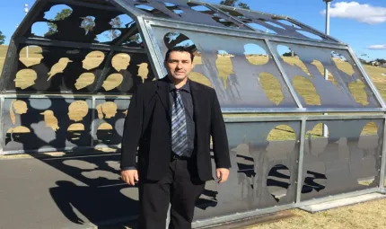 An Aboriginal man in a suit standing in front of a large outdoor metal sculpture.